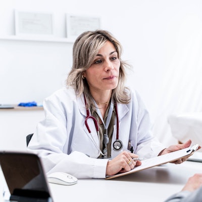 Eine Ärztin sitzt im Behandlungszimmer einer Praxis und hört ihrem Patienten zu