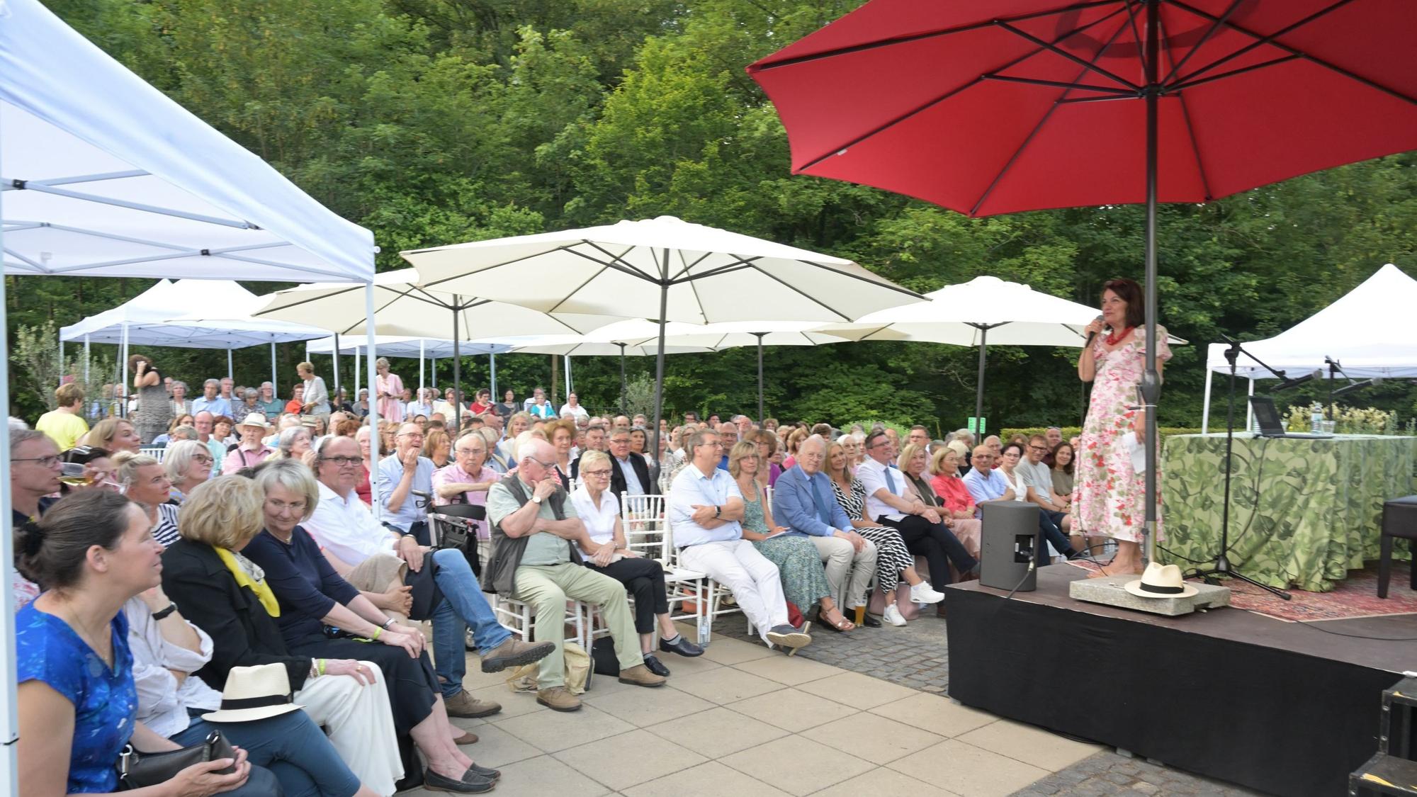 Eine Bühne unter großen Sonnenschirmen. Auf der Bühne spricht eine Frau in ein Mikrofon.
