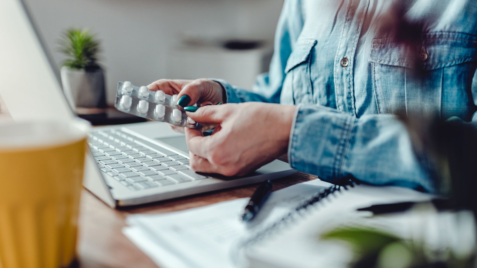 Eine Frau sitzt vor dem Laptop im Home Office und nimmt Tabletten.