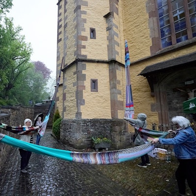 Einige Menschen stehen vor der Kirche und breiten den langen Wollschal aus.