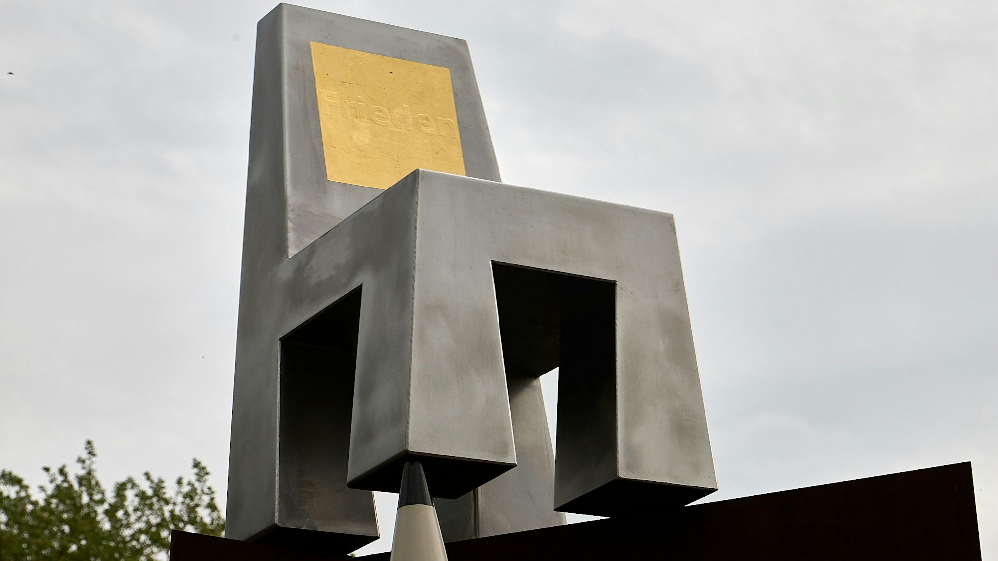 Auf der Rückenlehne des silbernen Stuhle ist eine goldene Plette eingelassen, in der das Wort „Frieden“ steht.