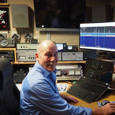 Funker Klaus Baer inmitten seines Equipments, das um ihn herum steht.