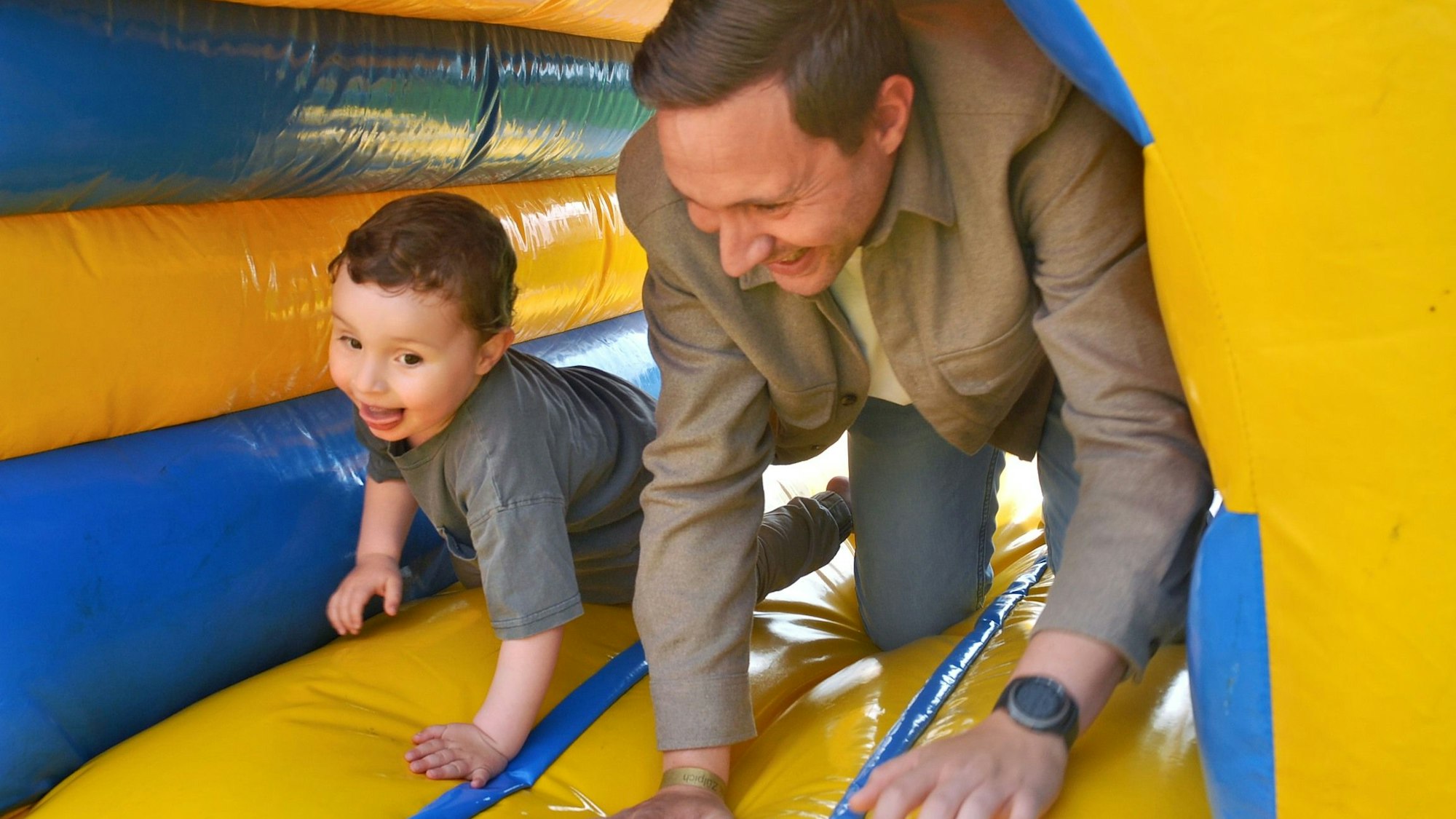 Ein kleiner Junge kriecht mit seinem Vater durch einen Tunnel einer Hüpfburg. Beide haben sichtlich Spaß.