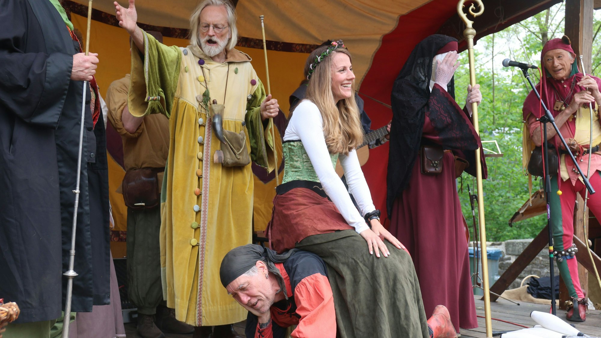 Eine junge Frau im Mittelaltergewand sitzt auf einem Mann, der sich auf allen Vieren hingehockt hat.