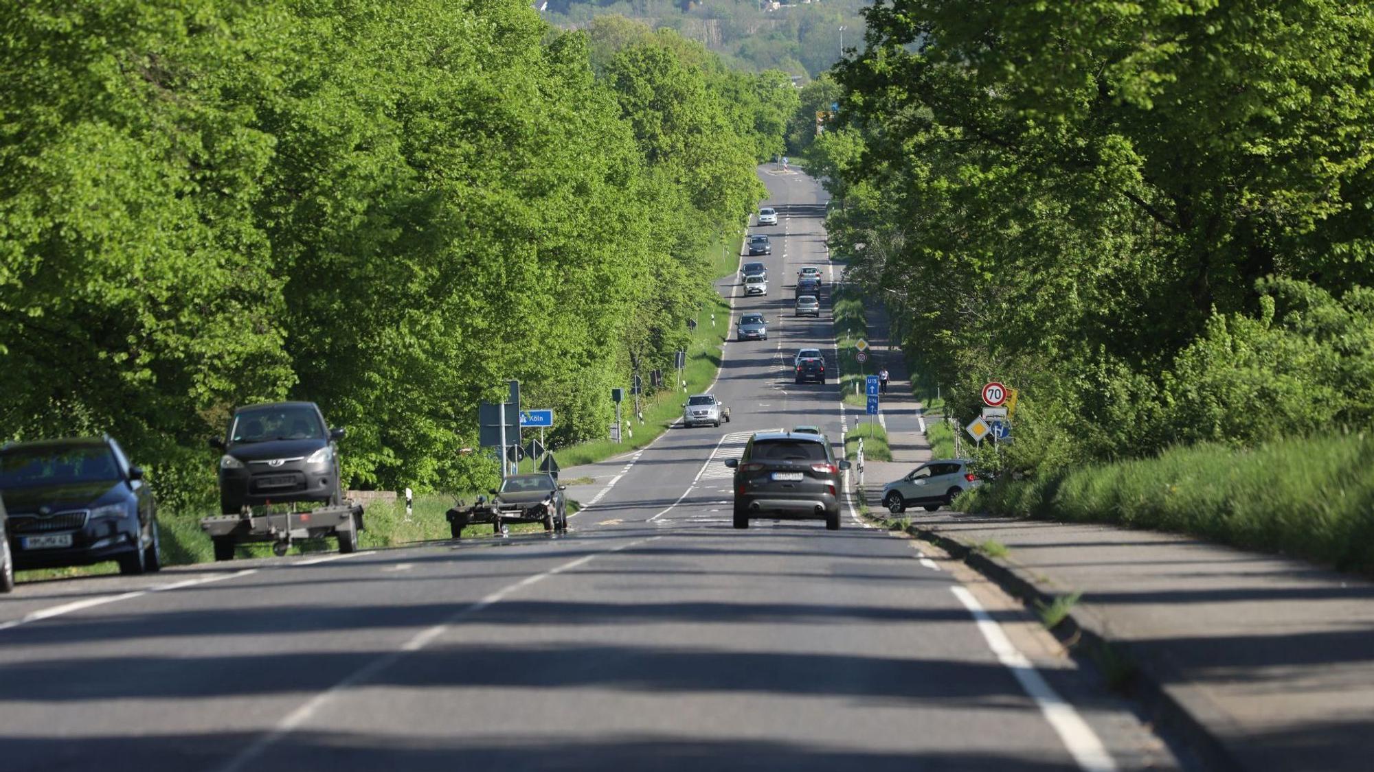 Eine langgezogene Straße mit mehreren Autos, einige Fahrzeuge parken links am Fahrbahnrand.