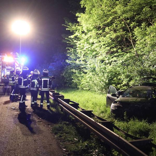 Der Scheinwerfer auf einem Feuerwehrwagen leuchtet die Unfallstelle aus, der beschädigte Pkw steht im Grünstreifen hinter der Leitplanke.