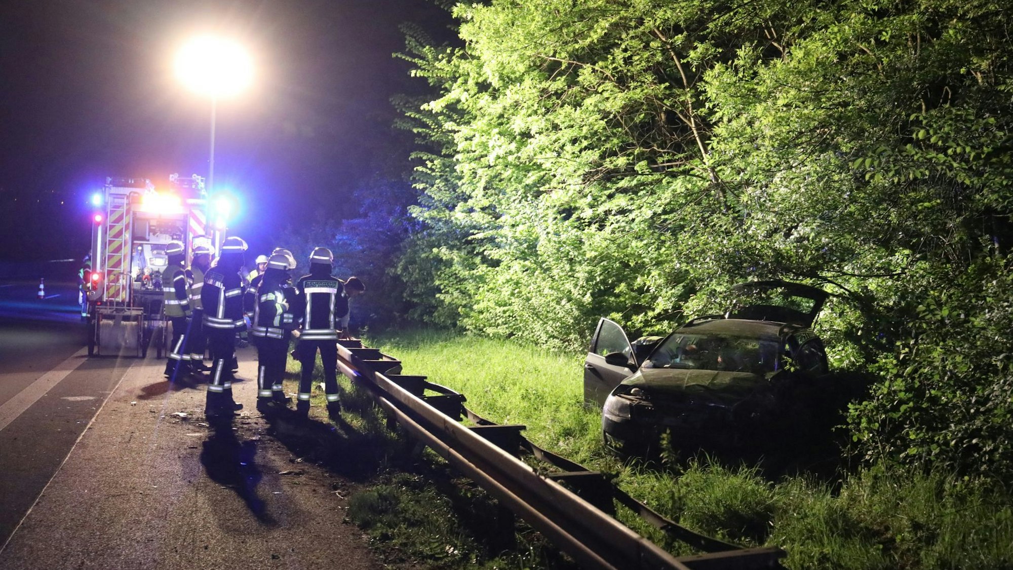 Der Scheinwerfer auf einem Feuerwehrwagen leuchtet die Unfallstelle aus, der beschädigte Pkw steht im Grünstreifen hinter der Leitplanke.
