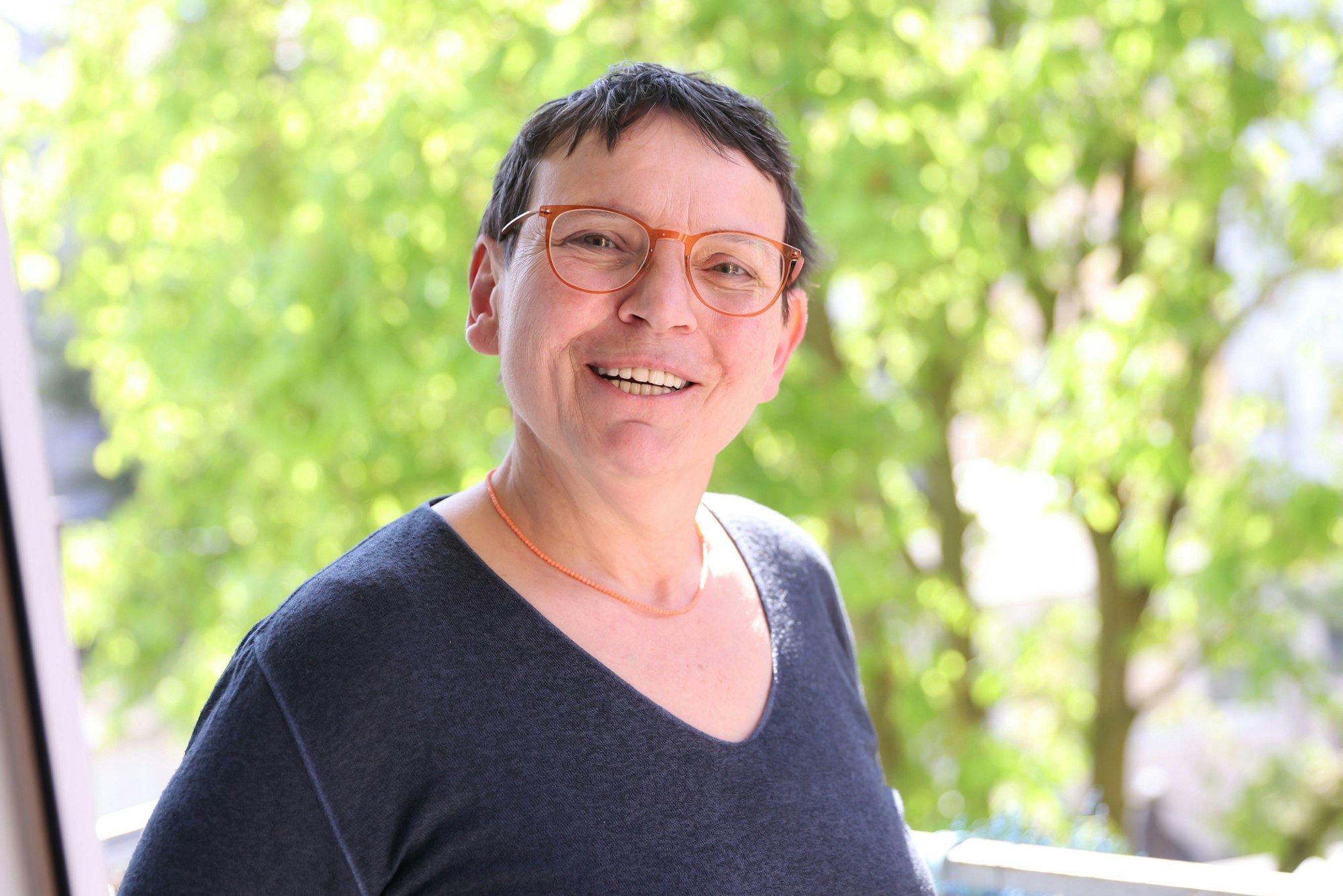 Susanne Bösel schaut offen und lächelnd in die Kamera. Im Hintergrund sind Bäume zu sehen.