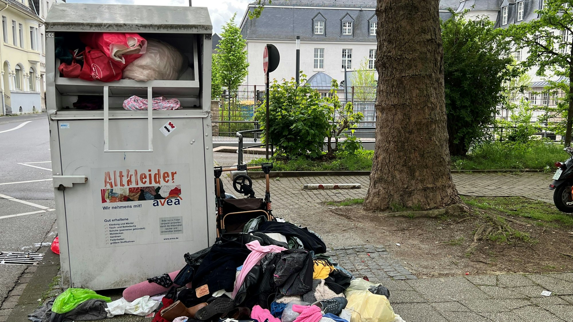 Ein überquellender Altkleider-Container mit davor abgelegten Altkleidern.