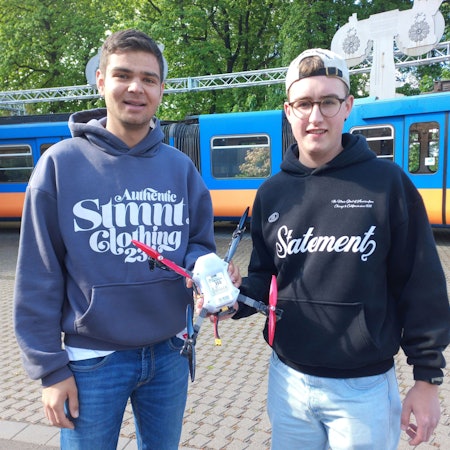 Zwei junge Männer halten eine Drohne in den Händen.