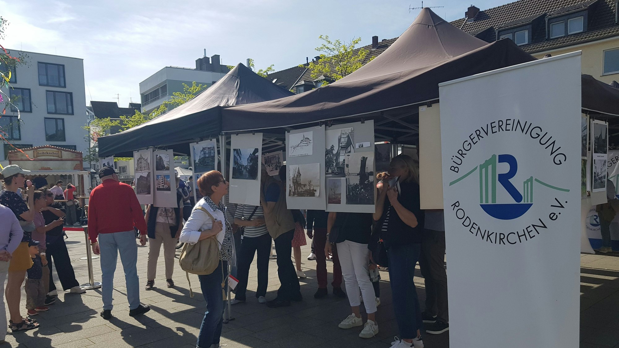 Menschen stehen vor Bildern, die unter einem Pavillon auf einem Platz aufgehängt wurden.