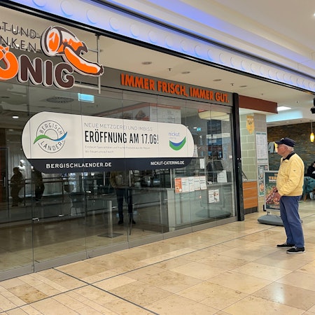 Ein Mann steht vor einer Schaufenster-Scheibe mit einer Geschäftsankündigung.