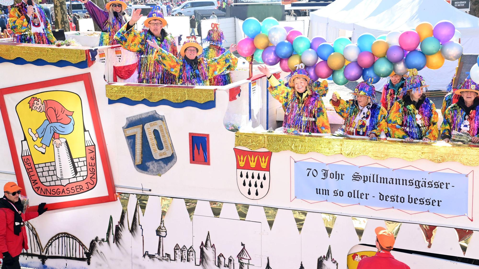 Ein Karnevalswagen, geschmückt mit Luftballons und bunt gekleideten Frauen, die darauf fahren, ist zu sehen.