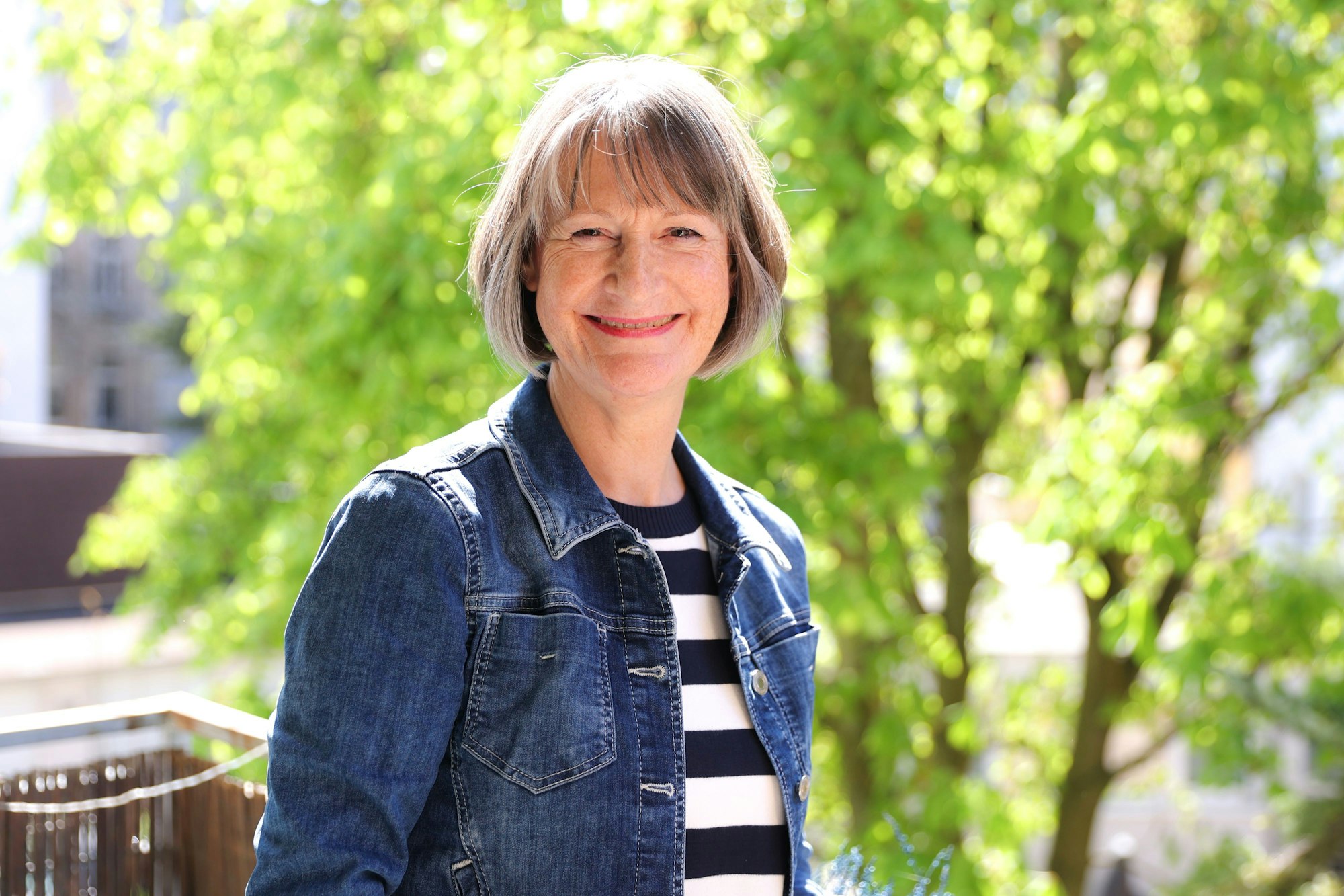Kirsten Hahn ist vor einem sonnenbeschienenen Baum zu sehen. Sie lacht in die Kamera.