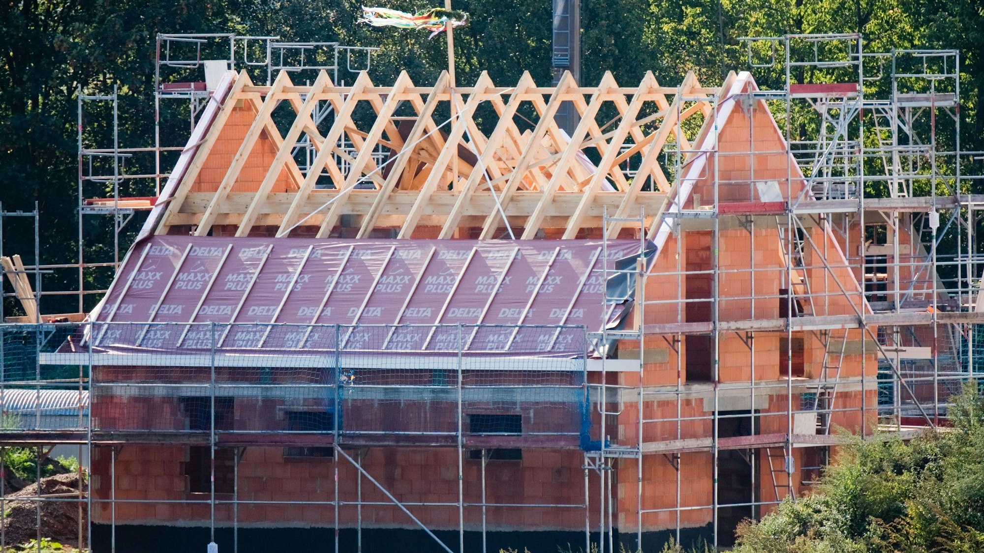 Ein Richtkranz weht am Dachstuhl eines neu gebauten Einfamilienhauses in einer Neubausiedlung.