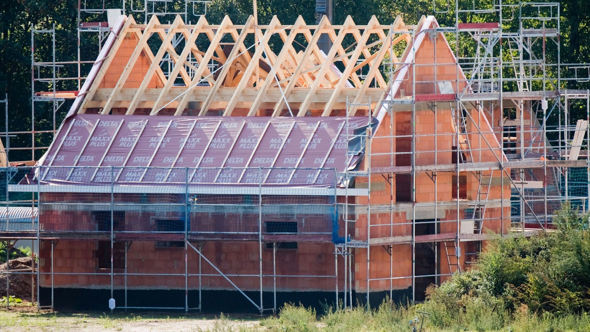 Ein Richtkranz weht am Dachstuhl eines neu gebauten Einfamilienhauses in einer Neubausiedlung.