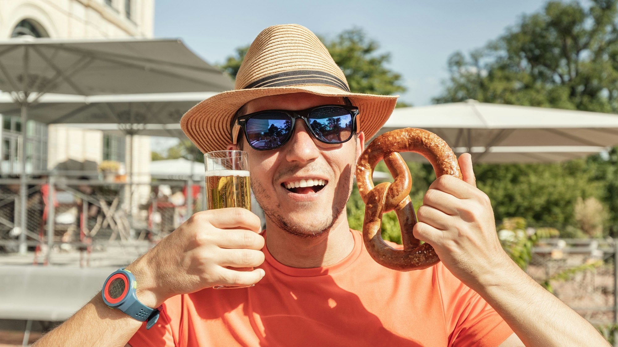 Mann mit einem Glas Bier und einer traditionellen deutschen Brotzeitbrezel in einem Biergarten oder einer Bar im Freien.