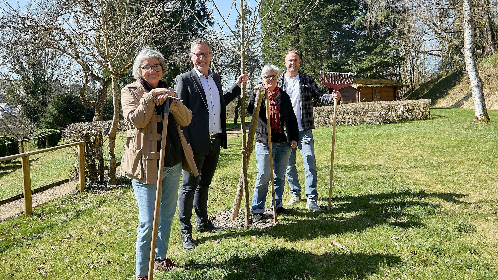 Zwei Frauen und zwei Männer stehen in Nettersheim auf einer Wiese an frisch gepflanzten Bäumen.