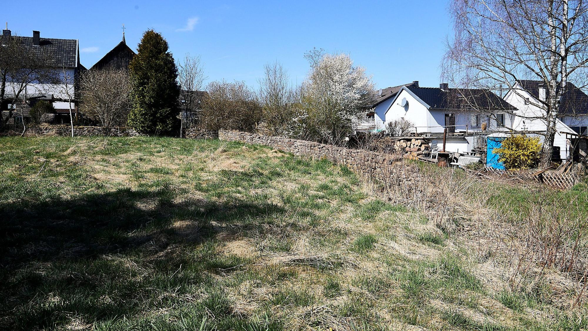 Die Wiese ist der ehemalige Friedhof von Nettersheim. Im Hintergrund sind einige Häuser des Ortes zu sehen.