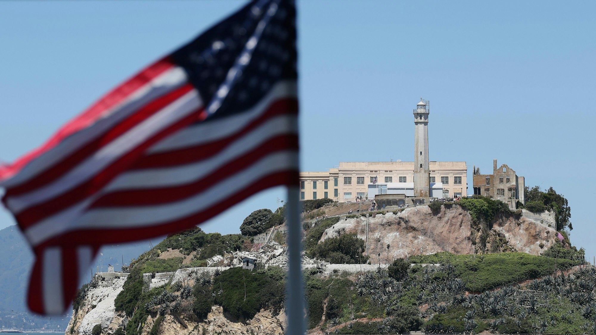 05.05.2025, USA, San Francisco: Eine US-amerikanische Flagge weht auf der Rückseite einer Fähre vor der Insel Alcatraz in San Francisco. US-Präsident Trump will das berüchtigte Gefängnis Alcatraz wieder in Betrieb nehmen und dort künftig Schwerverbrecher unterbringen. Foto: Jed Jacobsohn/FR170650 AP/AP/dpa +++ dpa-Bildfunk +++