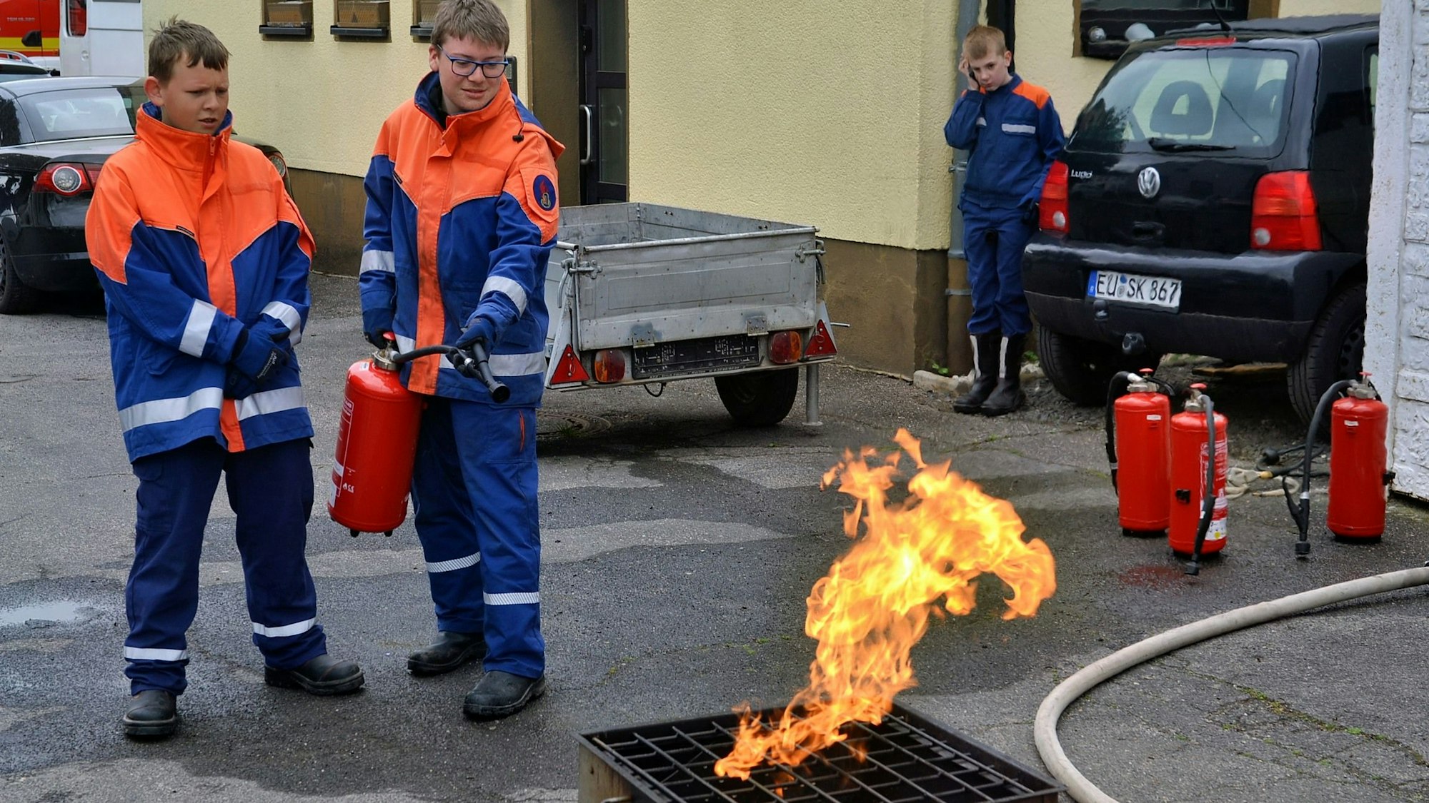 Zwei Mitglieder der Jugendfeuerwehr stehen bereit, um im Rahmen einer Vorführung einen kleinen Brand mit einem Feuerlöscher zu bekämpfen.
