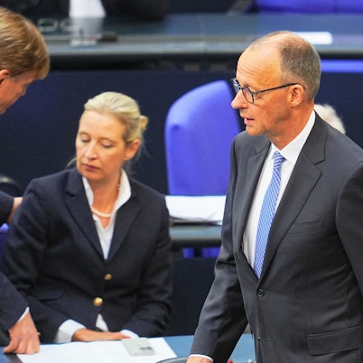 Friedrich Merz geht am Dienstag durch den Bundestag. Im Hintergrund ist AfD-Chefin Alice Weidel zu sehen.