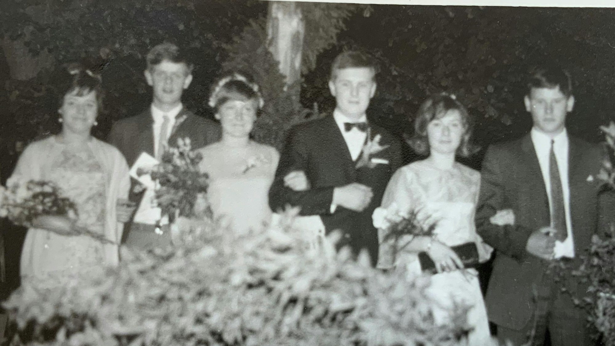 Auf einer Schwarzweiß-Fotografie präsentieren sich drei Maipaare aus dem Jahr 1968. Die jungen Frauen tragen festliche Kleider, Blumenschmuck im Haar sowie Blumensträuße, die jungen Männer tragen Anzug und Krawatte.