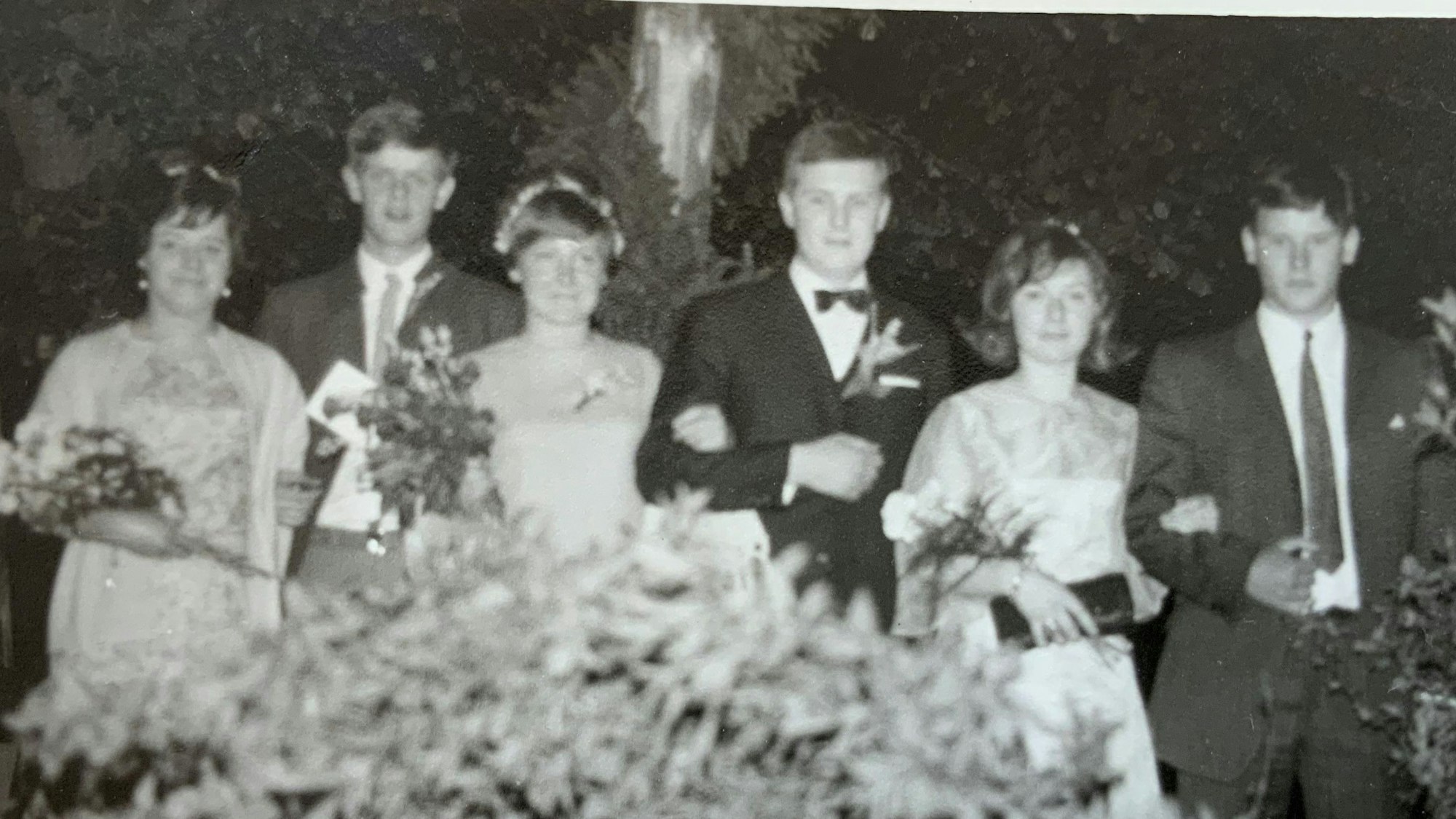 Auf einer Schwarzweiß-Fotografie präsentieren sich drei Maipaare aus dem Jahr 1968. Die jungen Frauen tragen festliche Kleider, Blumenschmuck im Haar sowie Blumensträuße, die jungen Männer tragen Anzug und Krawatte.