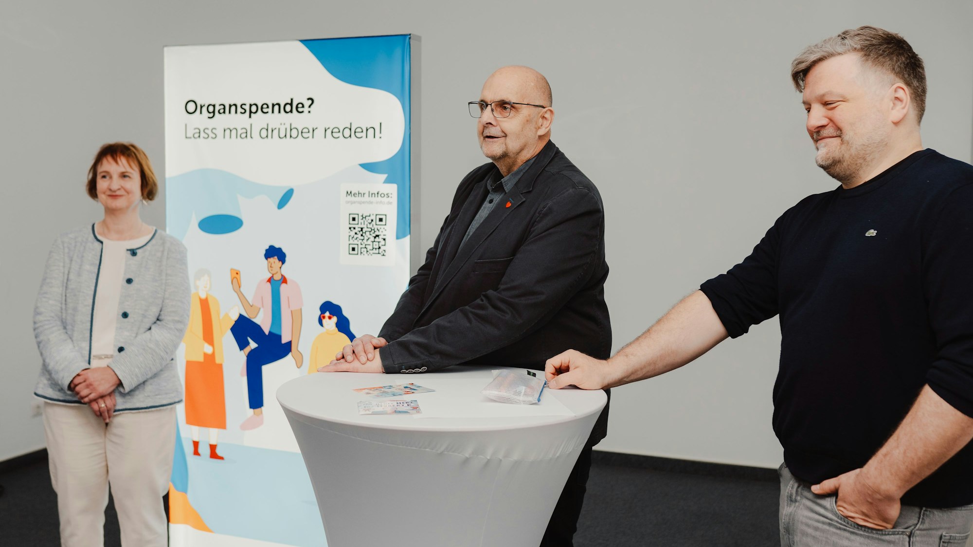 Bei der Vorstellung der Graphic Novel zur Organspende sind Knicker, der Zeichner und eine Frau vor einem Plakat zu sehen.