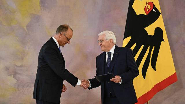 Friedrich Merz und Frank-Walter Steinmeier schütteln sich im Schloss Bellevue die Hände. Steinmeier hält Merz' Ernennungsurkunde in der Linken.