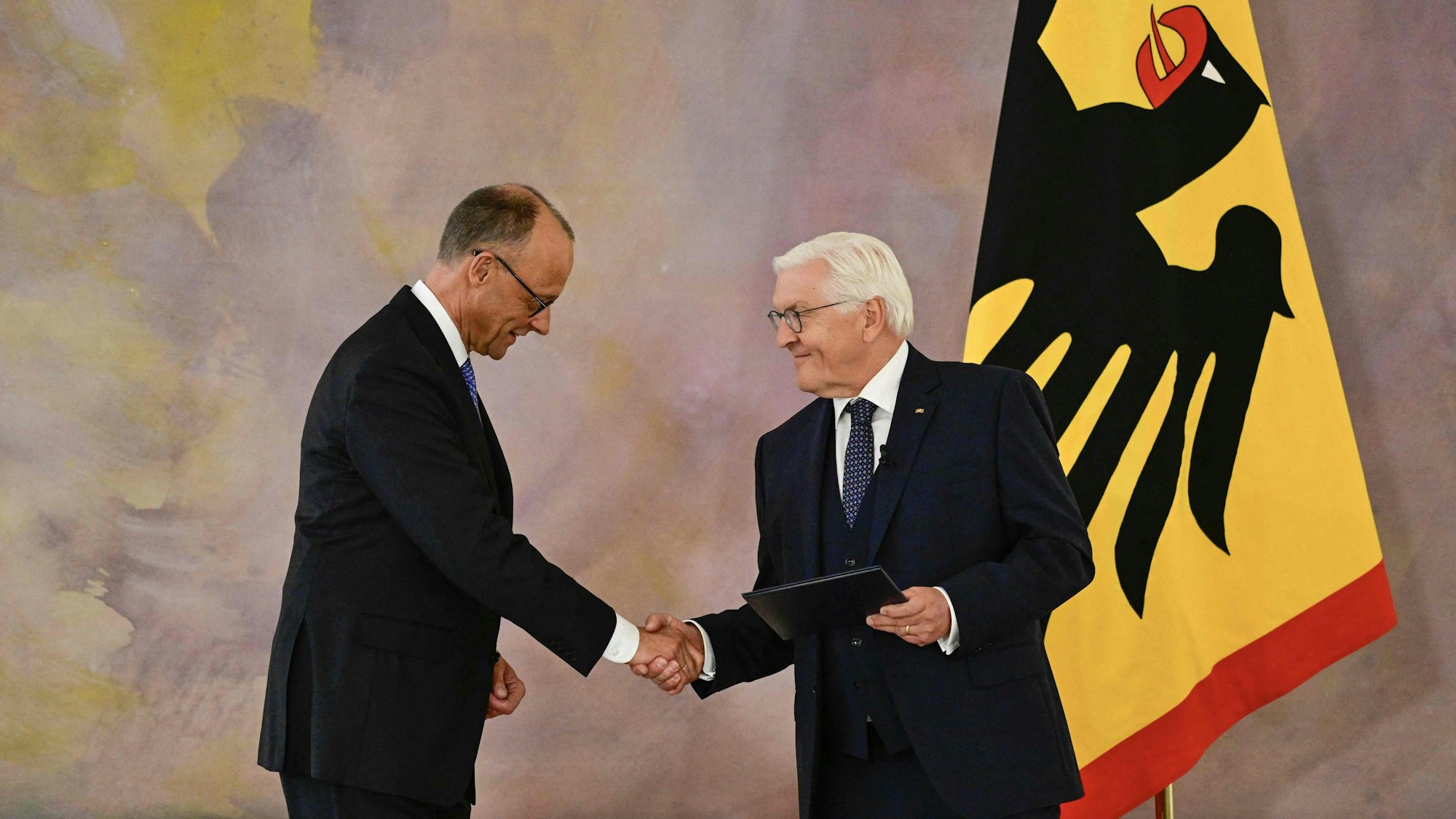 Friedrich Merz und Frank-Walter Steinmeier schütteln sich im Schloss Bellevue die Hände. Steinmeier hält Merz' Ernennungsurkunde in der Linken.