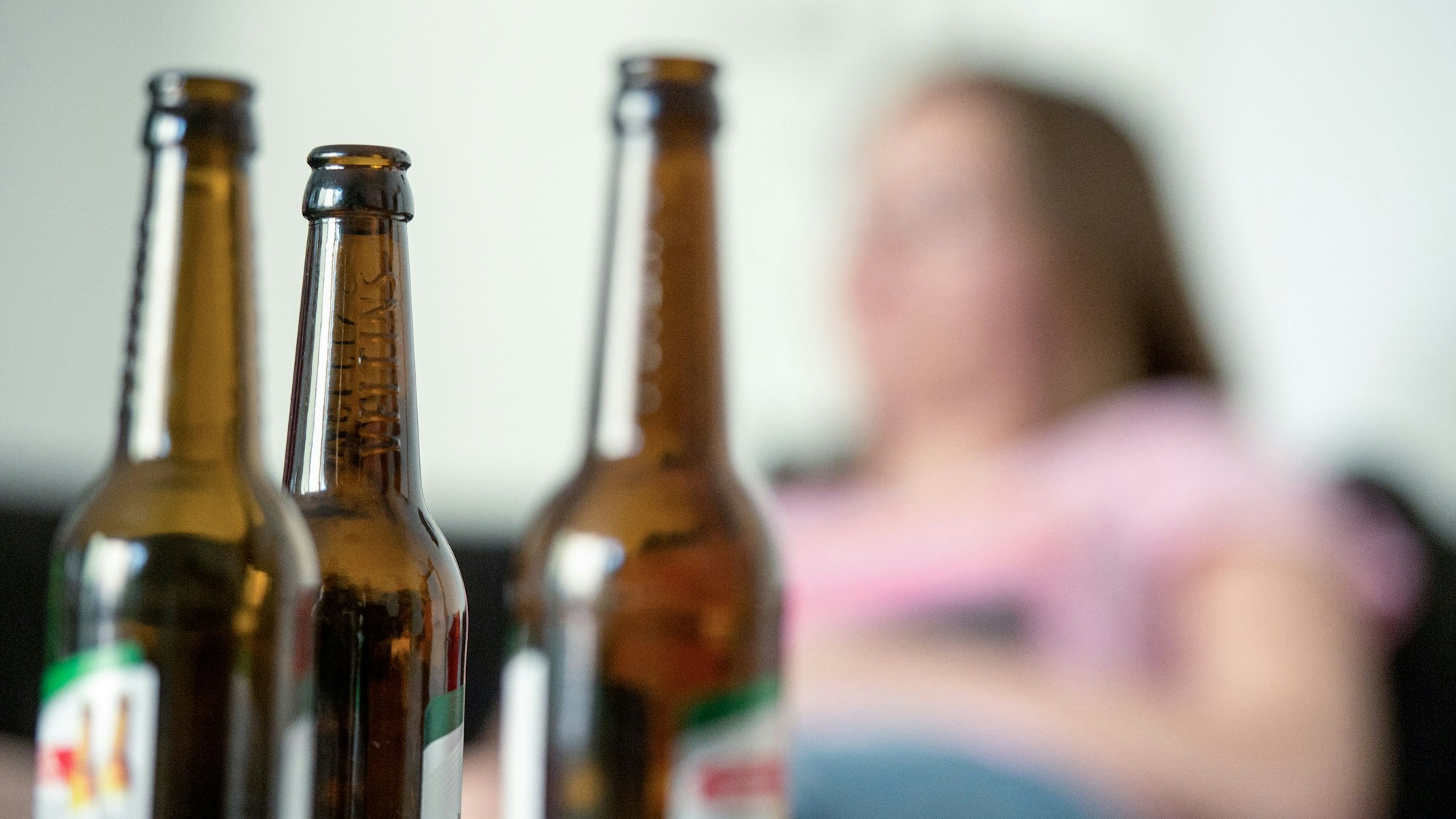 Eine junge Frau sitzt hinter leeren Bierflaschen.