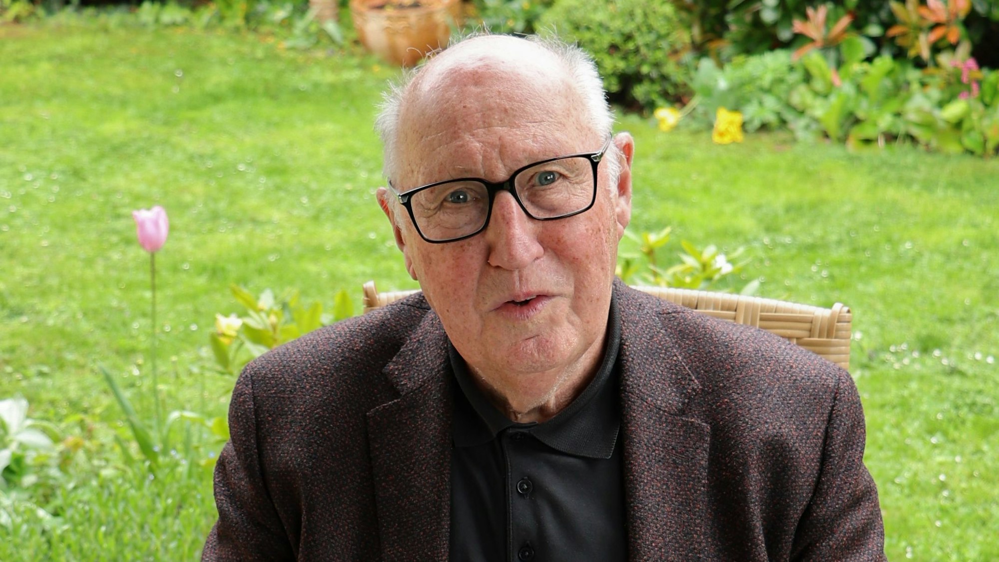 Dr. Günther Rüther, ein älterer Herr mit Brille, sitzt im Garten. Vor sich auf dem Tisch liegt das Buch, das er geschrieben hat.