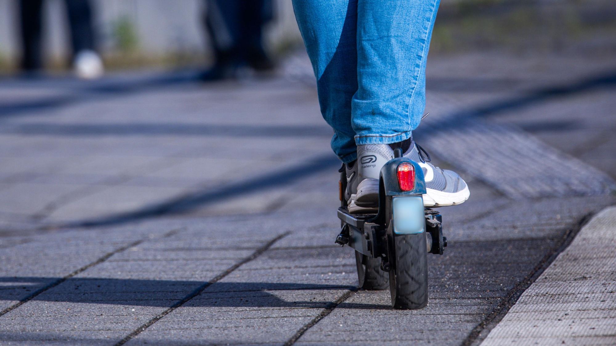 Das Foto zeigt die Beine eines Jugendlichen in Turnschuhen und Jeans, der auf einem E-Scooter fährt.
