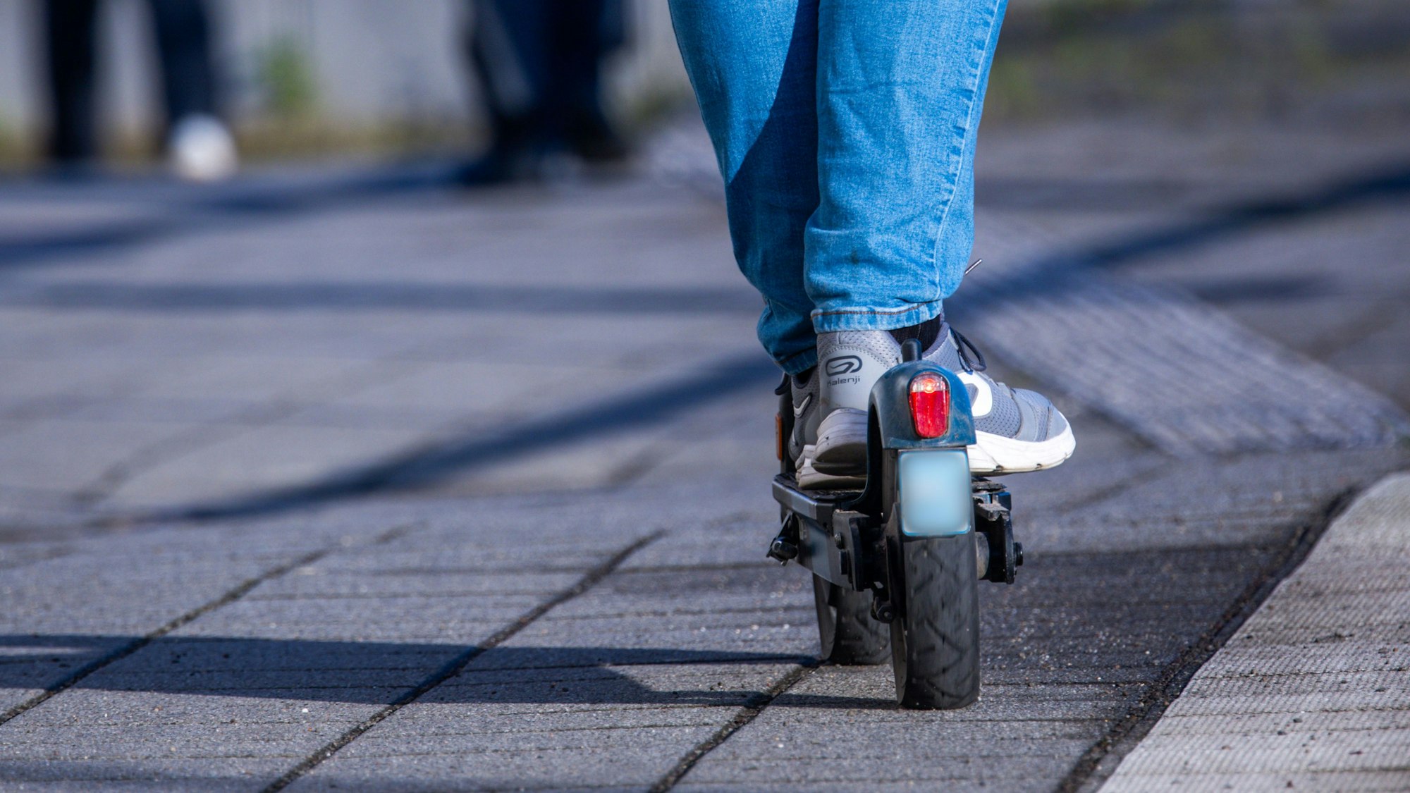 Das Foto zeigt einen Ausschnitt mit einer Person in Jeans und Turnschuhen auf einem E-Scooter.