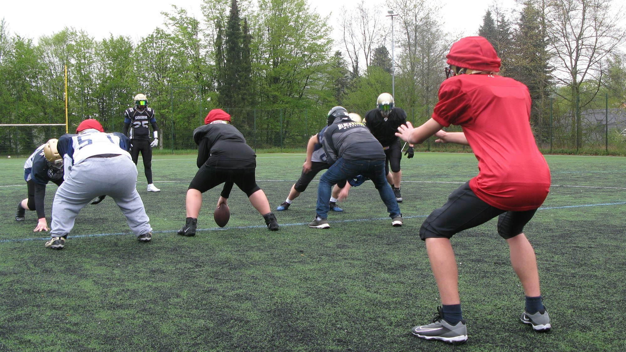 Der Quarterback im roten Trikot ist fangbereit, der Center snappt ihm den eiförmigen Ball zu.