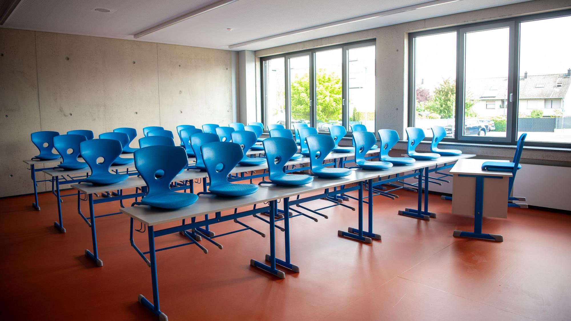 Blaue Stühle stehen auf Schultischen in einem frisch gebauten Klassenzimmer.