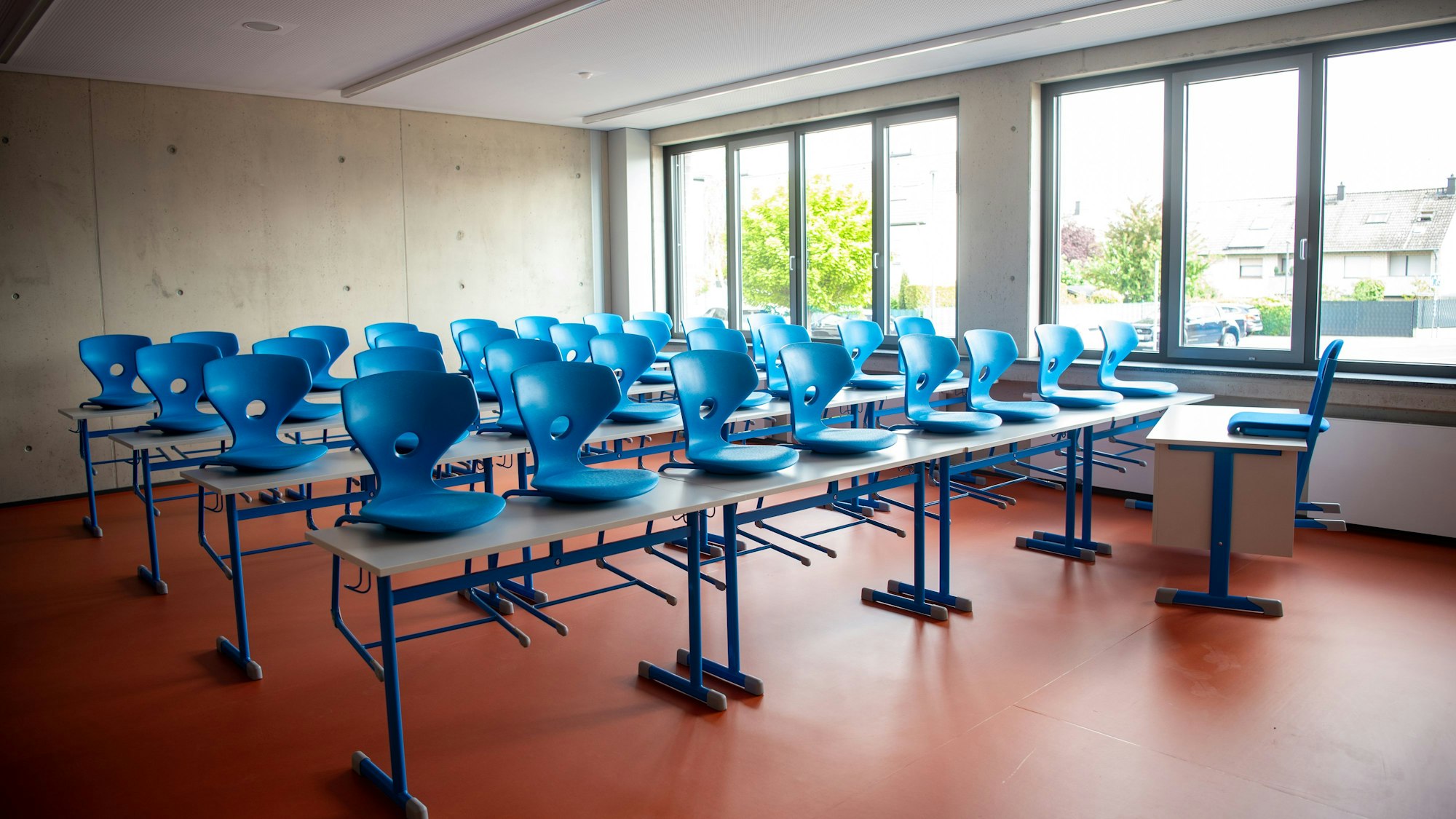 Blaue Stühle stehen auf Schultischen in einem frisch gebauten Klassenzimmer.