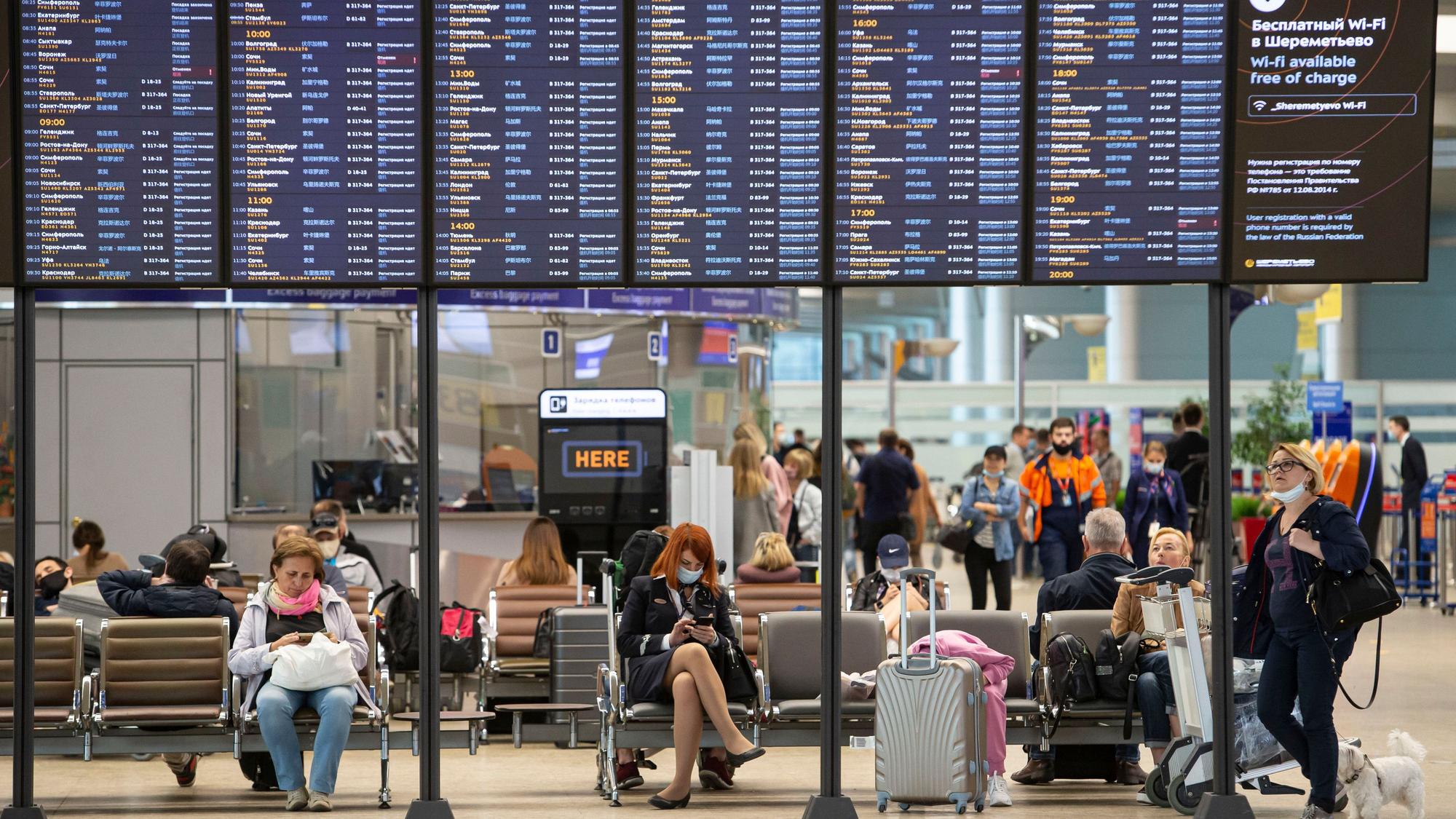 Passagiere sitzen auf dem internationalen Flughafen Scheremetjewo unter einer Fluginformationstafel.