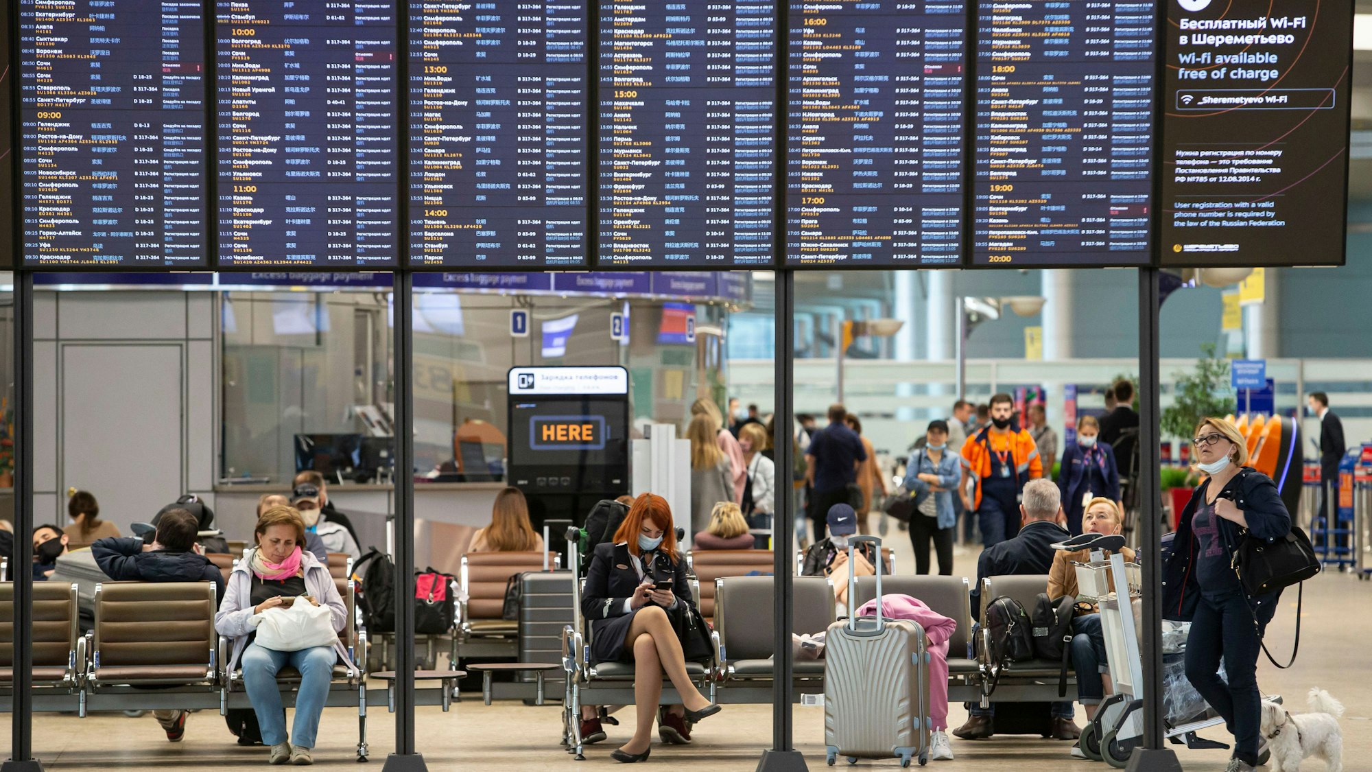 Passagiere sitzen auf dem internationalen Flughafen Scheremetjewo unter einer Fluginformationstafel.