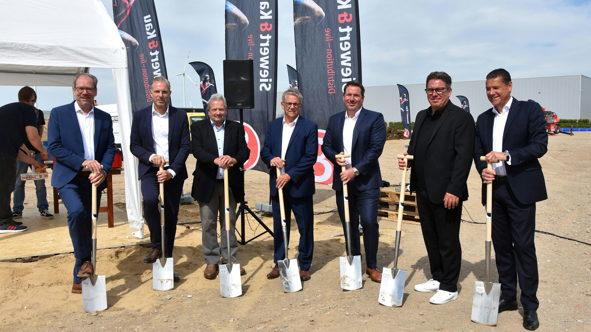 Auf dem Bild sind Männer in Anzügen zu sehen, die einen Spaten halten.