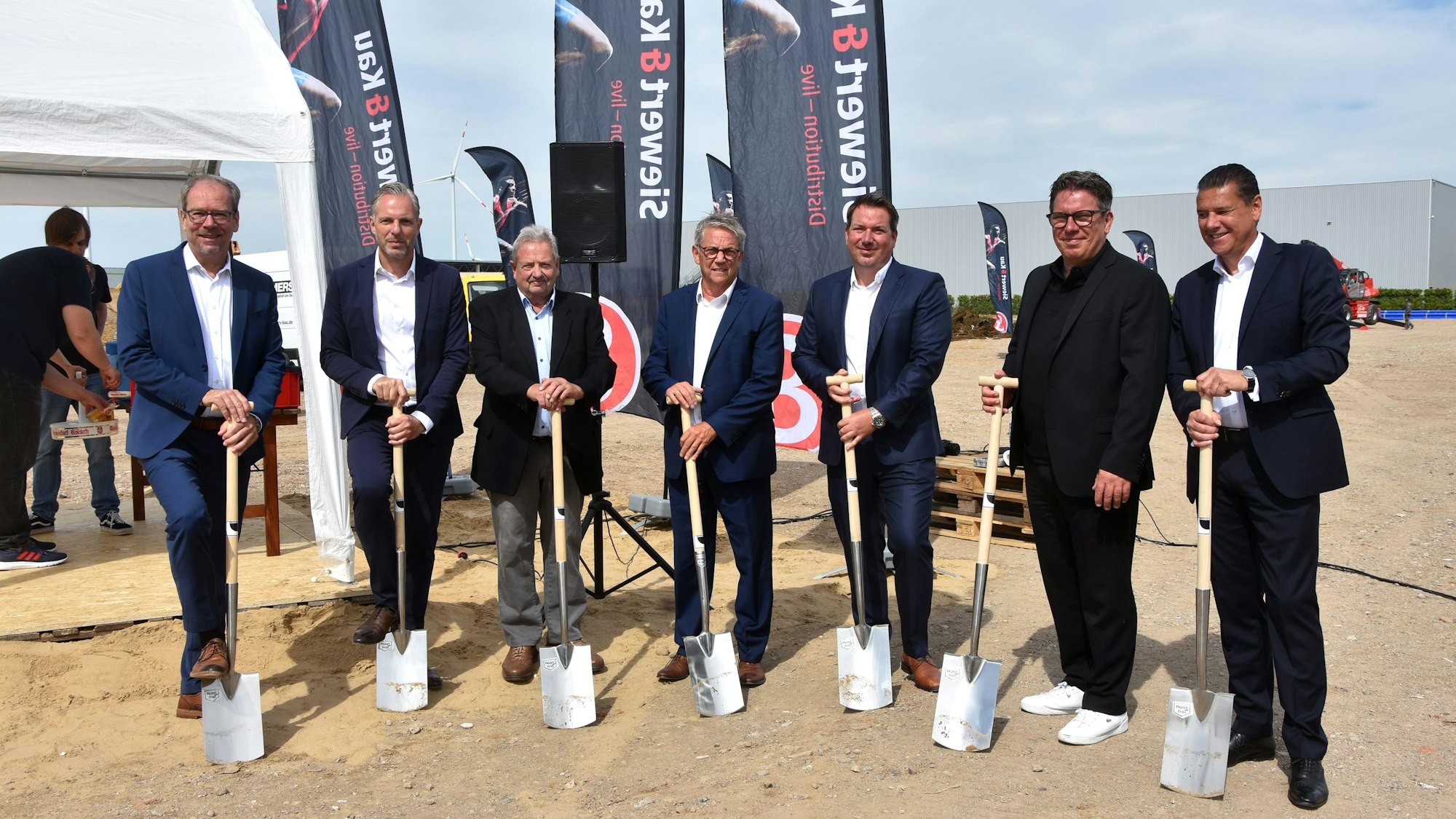 Auf dem Bild sind Männer in Anzügen zu sehen, die einen Spaten halten.