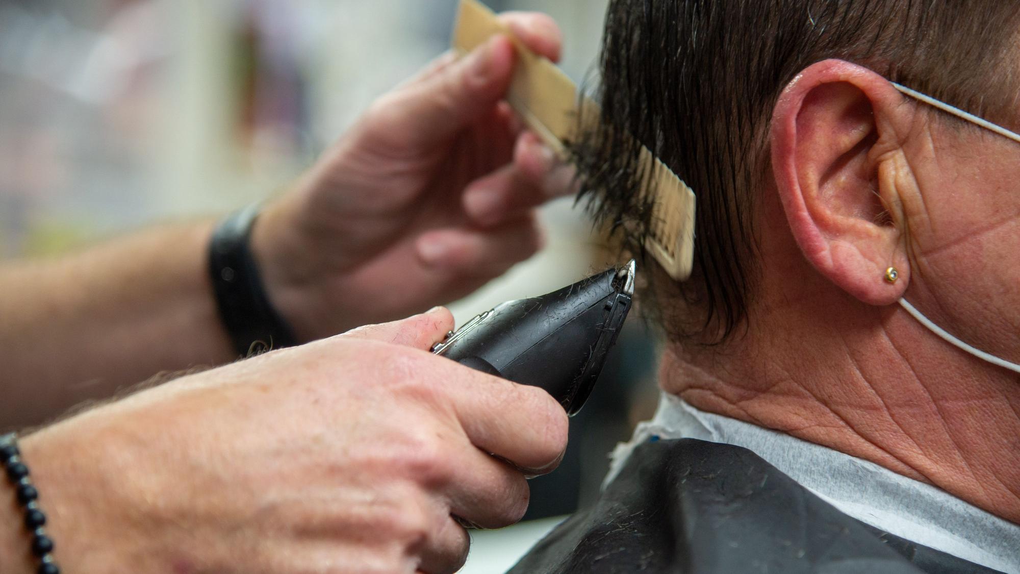 Mit Kamm und Rasierer ist ein Friseur an einer Herrenfrisur zugange.
