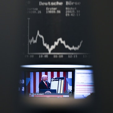 US-Präsident Trump ist auf einem Bildschirm auf dem Parkett der Frankfurter Wertpapierbörse vor der Anzeigetafel mit der Dax-Kurve zu sehen. Foto: Arne Dedert/dpa