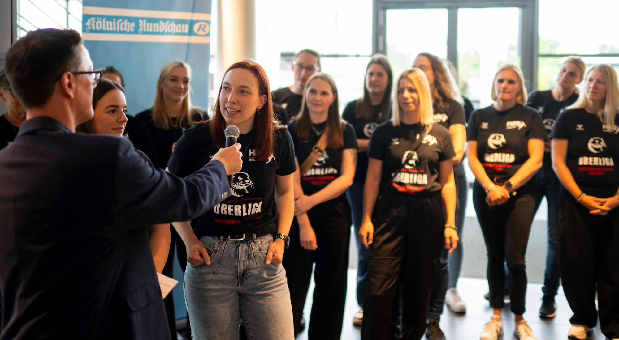 Lokalsportchef Thomas Schmitz interviewt Lea Schmitz bei der Sportlerwahl 2024. Die Mannschaft steht im Hintergrund.