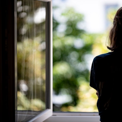 Frau steht an einem offenen Fenster (Symbolbild)
