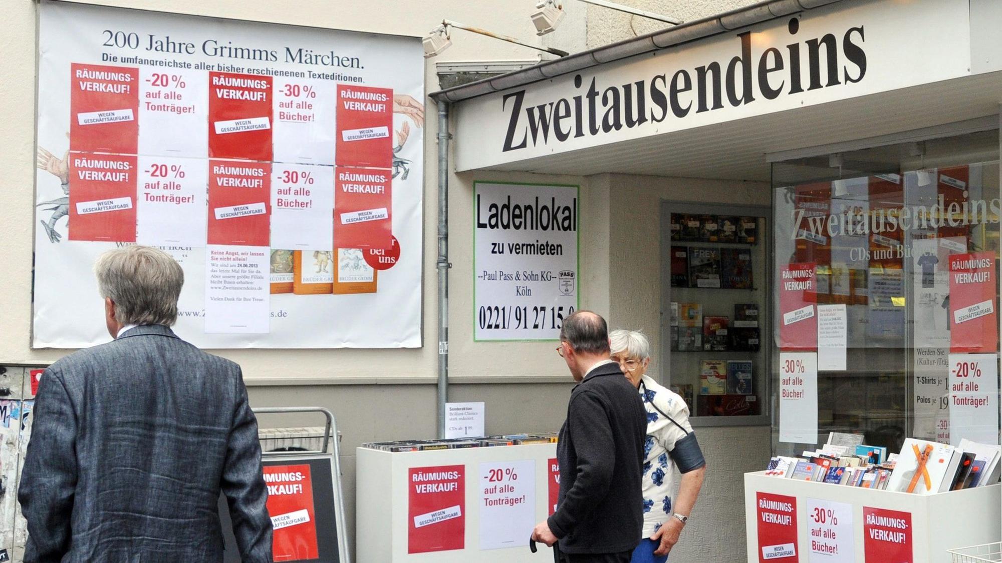 Vor der Fassade des Geschäfts Zweitausendeins stehen Menschen und begutachten Artikel in Kästen, auf denen „Räumungsverkauf“ geschrieben steht.