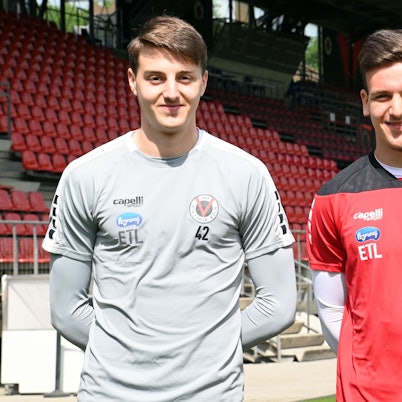 Zwei Fußballer stehen nebeneinander in einem Stadion.