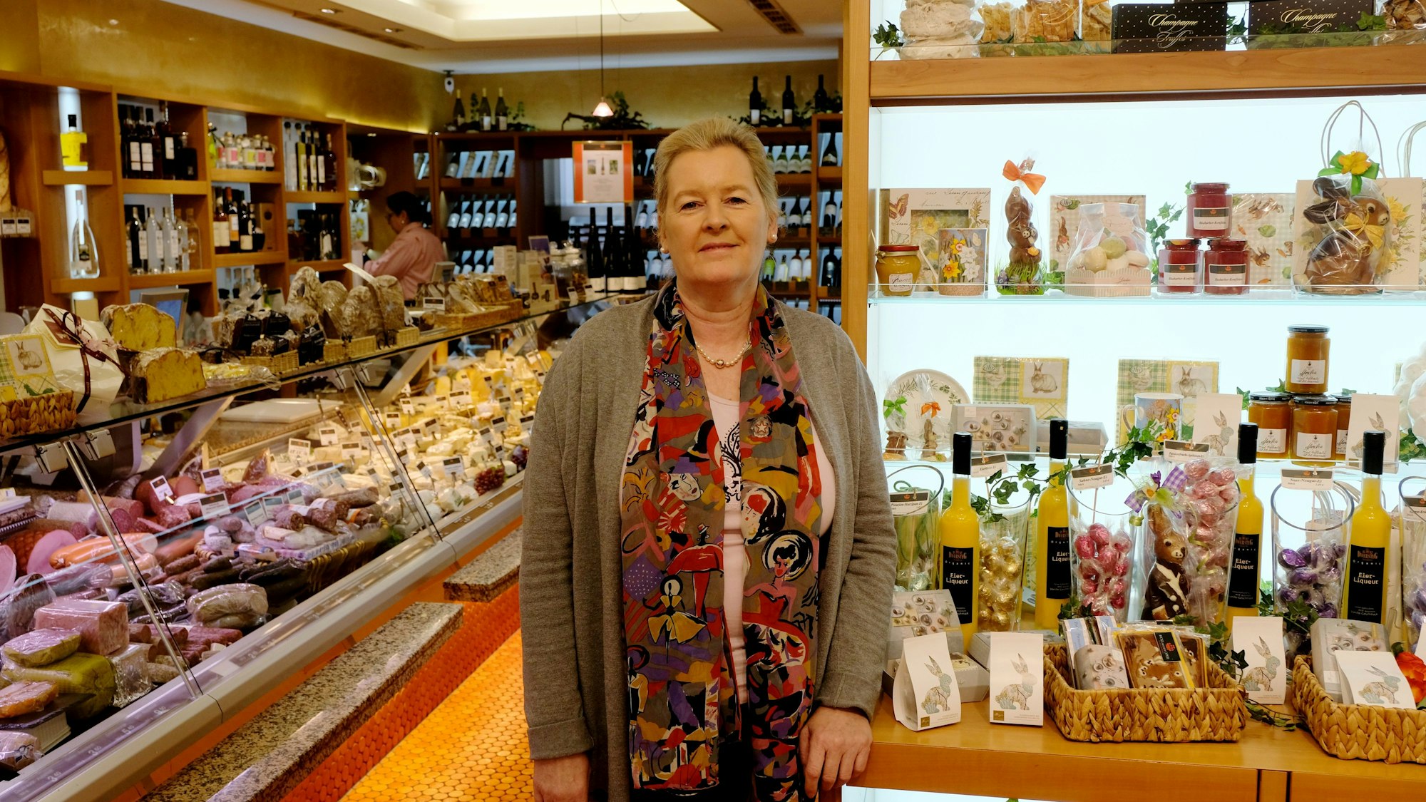 Petra Hoss-Müller lhent sich im Feinkostladen „Hoss an der Oper“ an eine Kommode. Es sind allerlei Essensprodulte zu sehen, unter anderem in einer Fleisch- und Käsetheke.