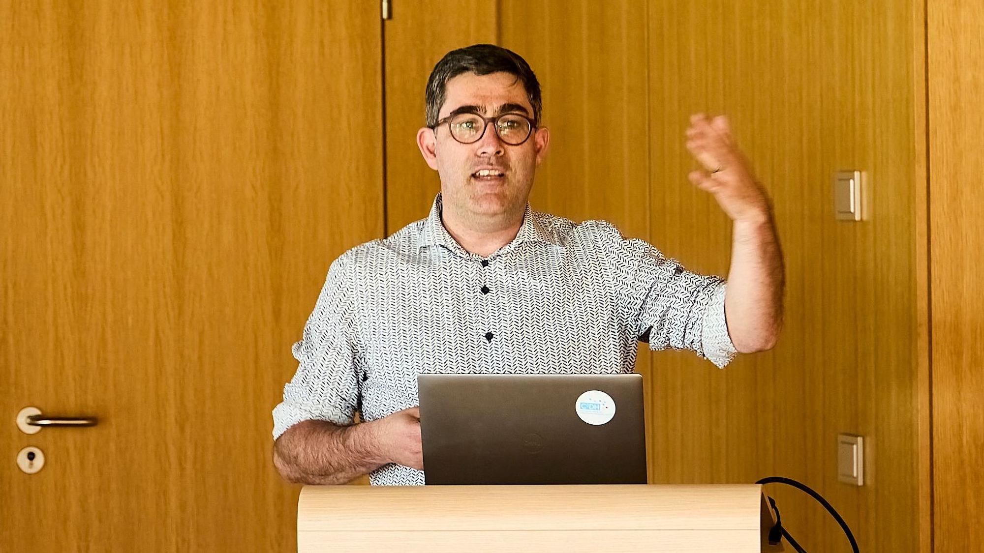 Professor Christoph Brüll steht in Vogelsang an einem Rednerpult und gestikuliert mit der linken Hand.